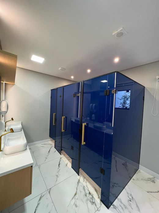 Banheiro coletivo com cabines de vidro azul e puxadores dourados
