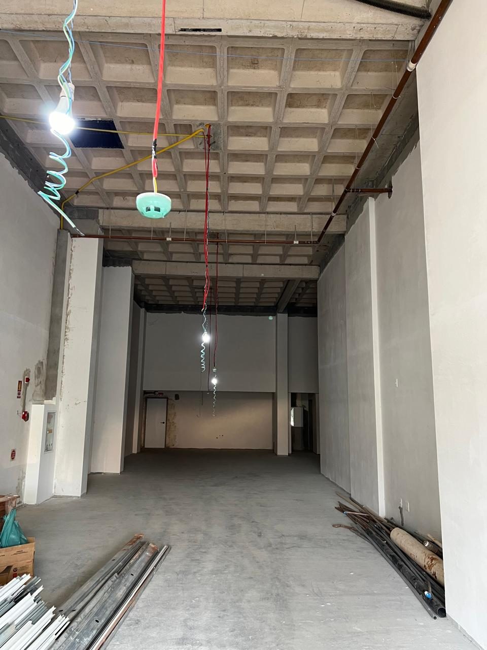 Antes: espaço comercial vazio em obra, com laje nervurada aparente e fios pendurados