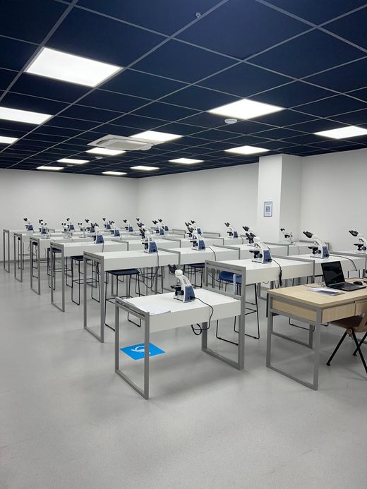 Laboratório de faculdade com bancadas brancas, microscópios e forro azul-marinho